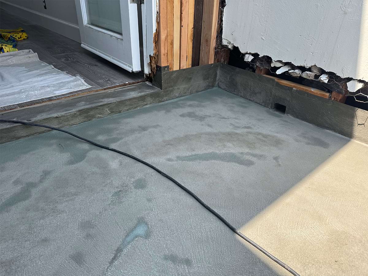 Concrete floor drying inside a partially exposed building wall. An open door and visible cable suggest ongoing renovation work.